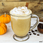 Vegan pumpkin spiced latte is a glass mug. Topped with whipped cream and a cinnamon stick.