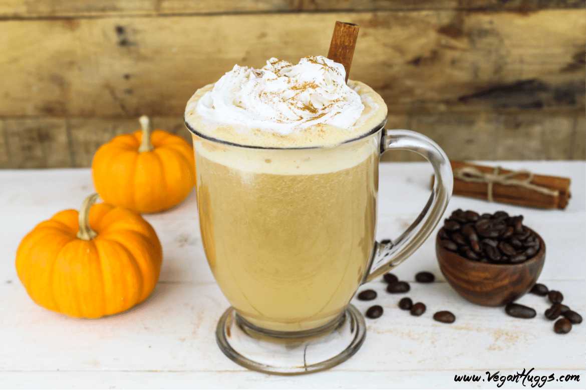 Vegan pumpkin spiced latte is a glass mug. Topped with whipped cream and a cinnamon stick.