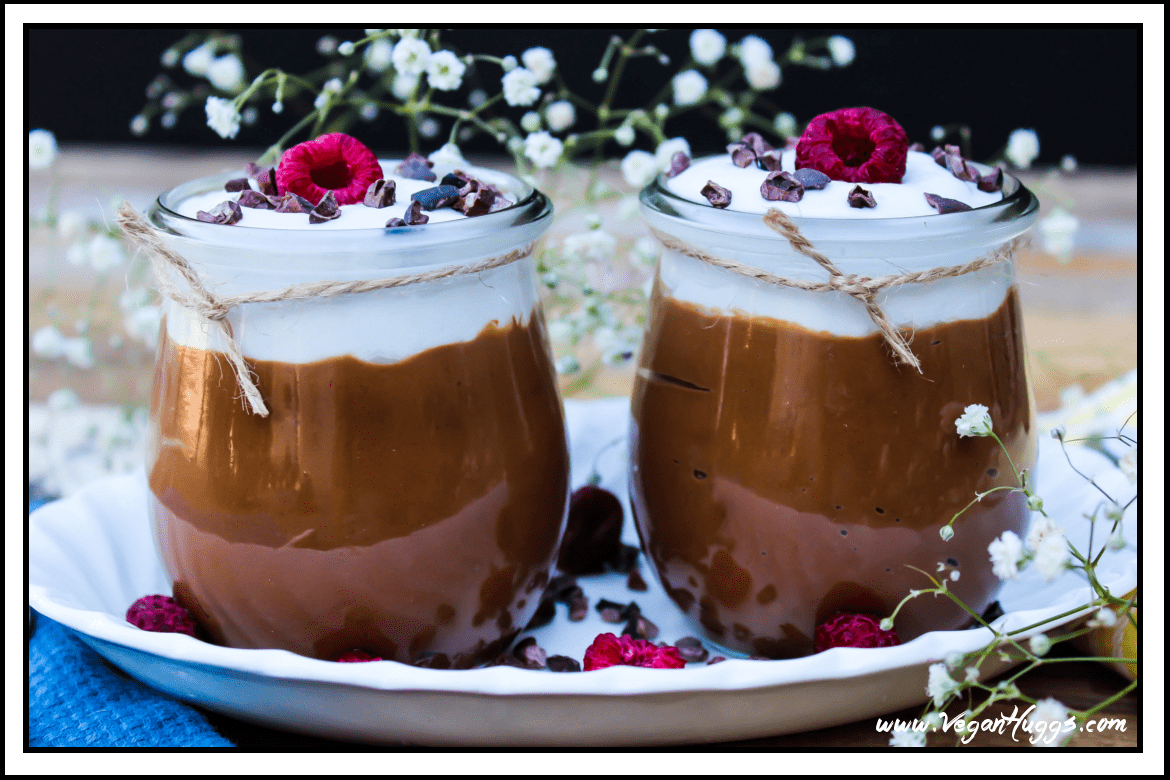 Two jars of dessert topped with whipped cream and raspberries. 