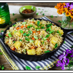 Fully cooked vegan pineapple fried rice in a cast iron skillet on a striped napkin. Purple and orange flowers on the side. 