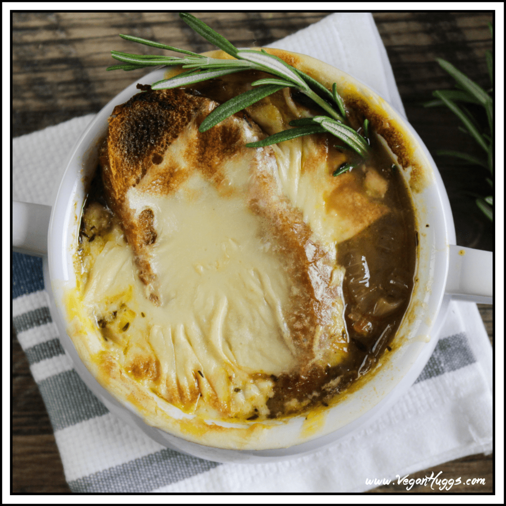 Overhead photo of vegan french onion soup in a white crock. Topped with vegan cheese and fresh rosemary.