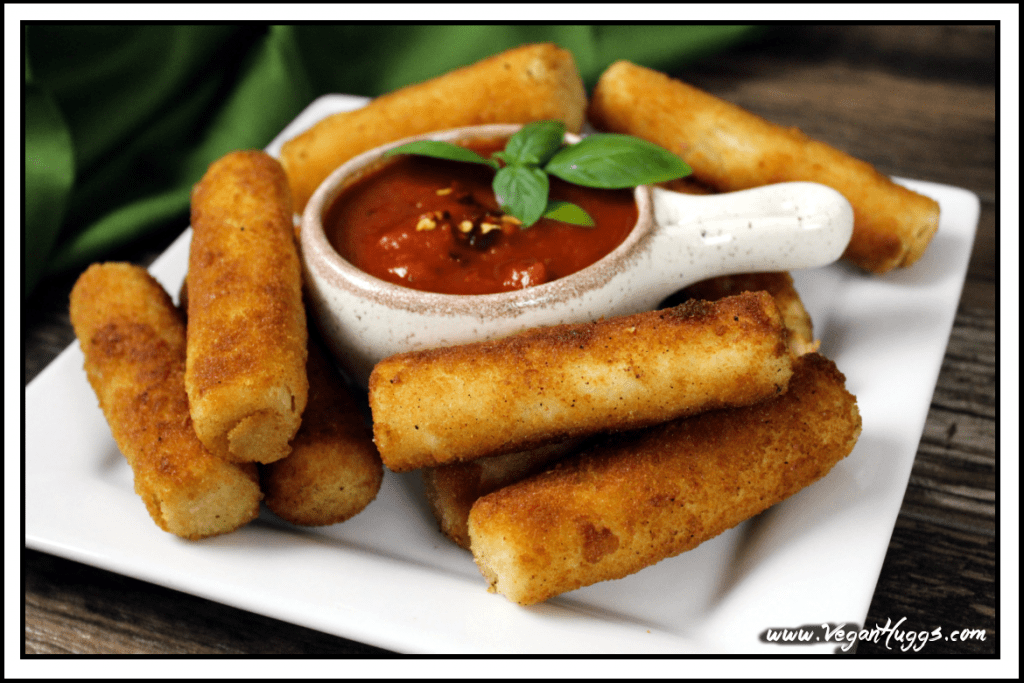 Side view of vegan mozzarella sticks on a white plate with sauce in the middle. 