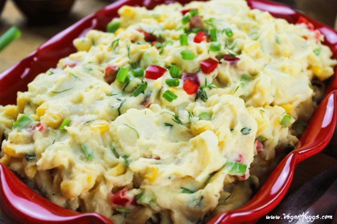 Closeup view of vegan potato salad in a red serving dish topped with fresh-cut herbs. 