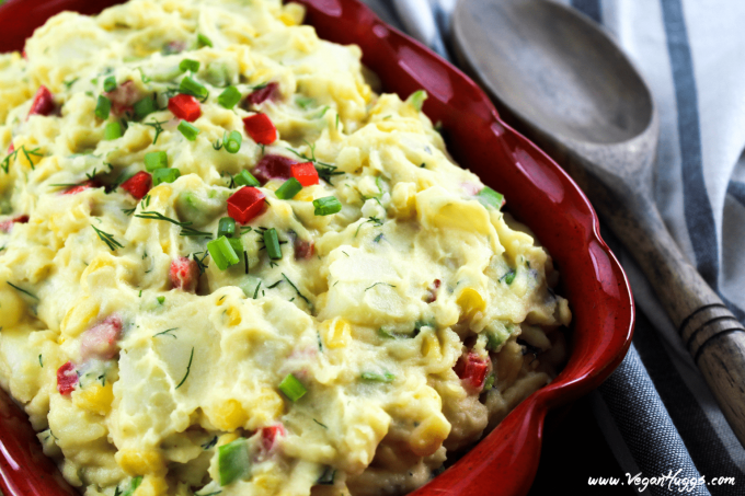 Side view of potato salad in a red dish with a wooden spoon on the side. 