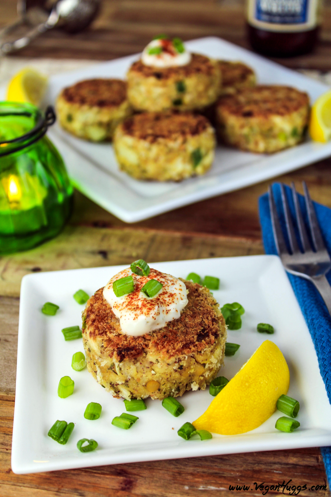 Vegan crab cakes on two serving plates. Green candle in the background with beverage. 