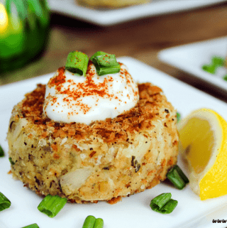 Vegan crab cakes on a white serving plate. Topped with tartar sauce, green onion and paprika.