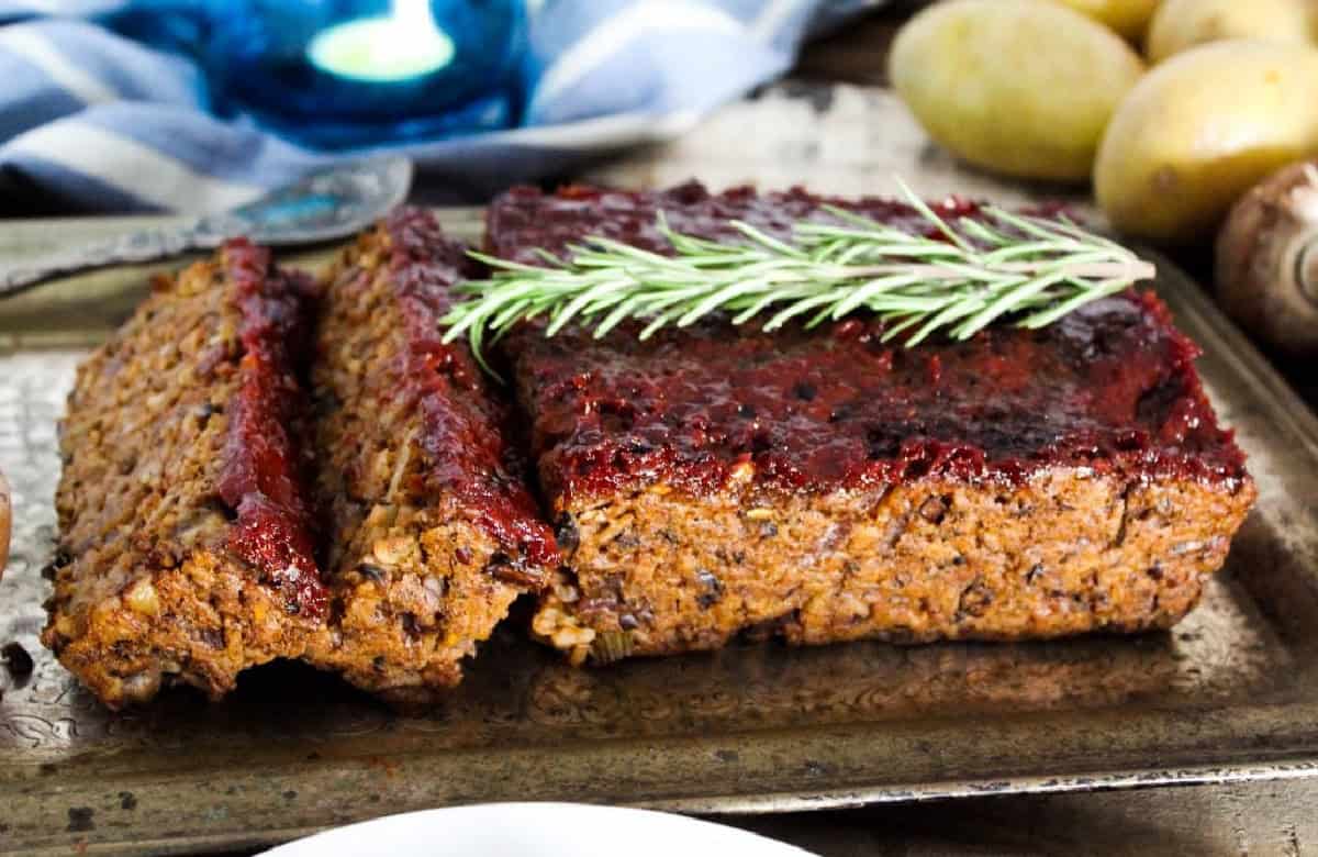 side view of vegan meatloaf with rosemary on a platter.