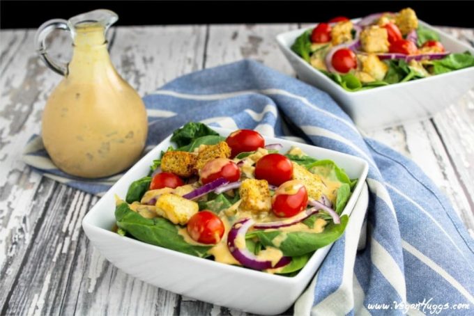 two bowls of salad with bottle of dressing on the side. 