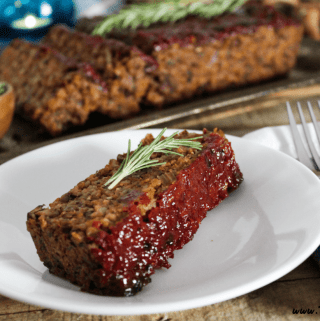 One slice of meatless loaf on a white plate. Full loaf in the background on s ilver serving tray.