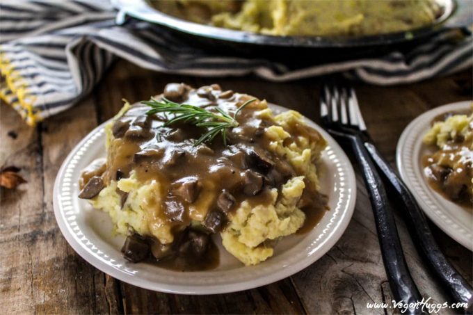 Two white plates of creamy mashed Potatoes toped with Mushroom Gravy. Two forks in the middle. 