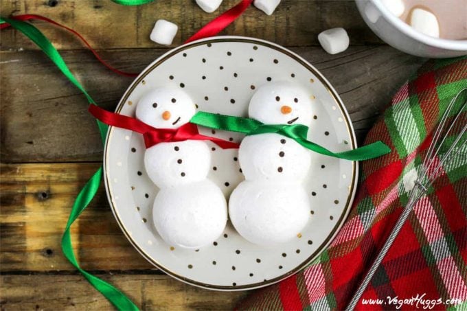 two snowmen meringue cookies on a polka dot plate. Hot cocoa on the side. 
