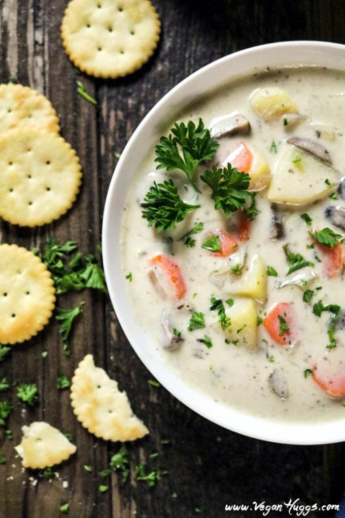 half view of vegan clam chowder in a white bowl with a line of crackers on the side. 