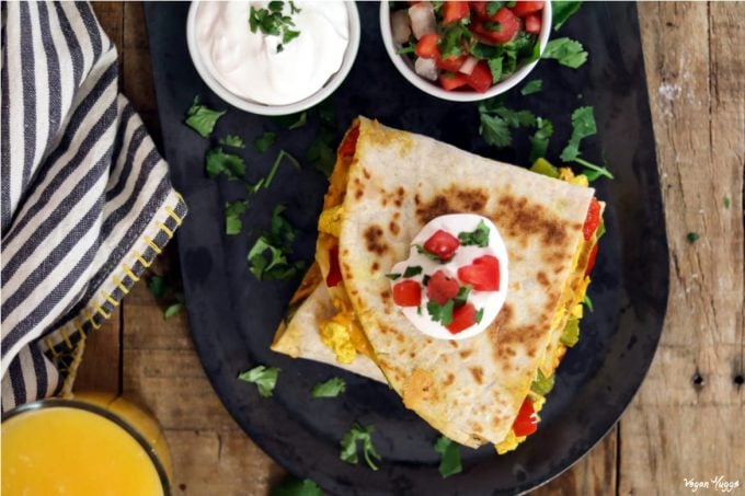 Overhead photo of vegan breakfast quesadilla topped with vegan sour cream, tomatoes and cilantro. 