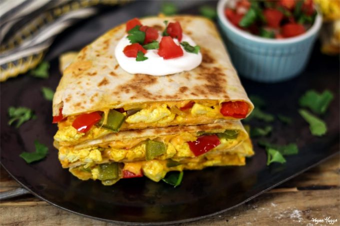 Side angle of vegan breakfast quesadilla topped with sour cream, tomatoes and cilantro. Side of pico de gallo. 