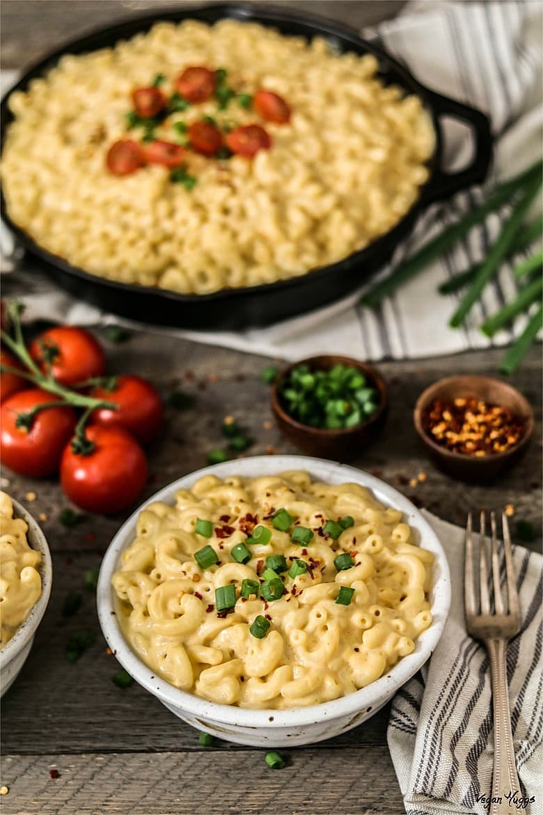 Vertical photo of cooked macaroni in white bowl. Filled cast iron skillet in background. 
