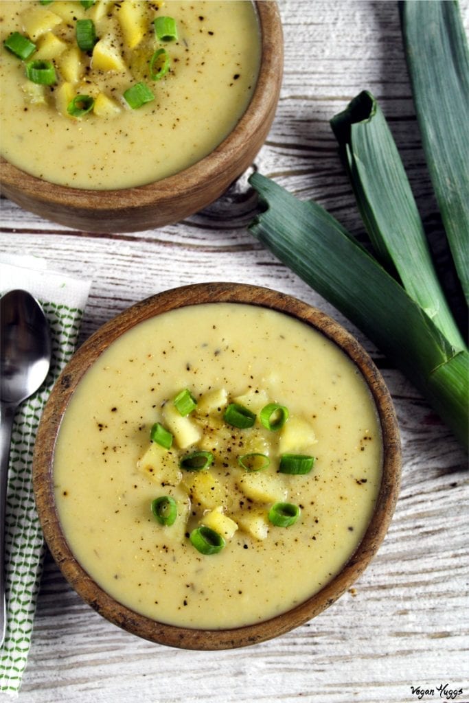 Overhead photo of two wooden bowls with filled with vegan potato leek soup. Large leek on the side.