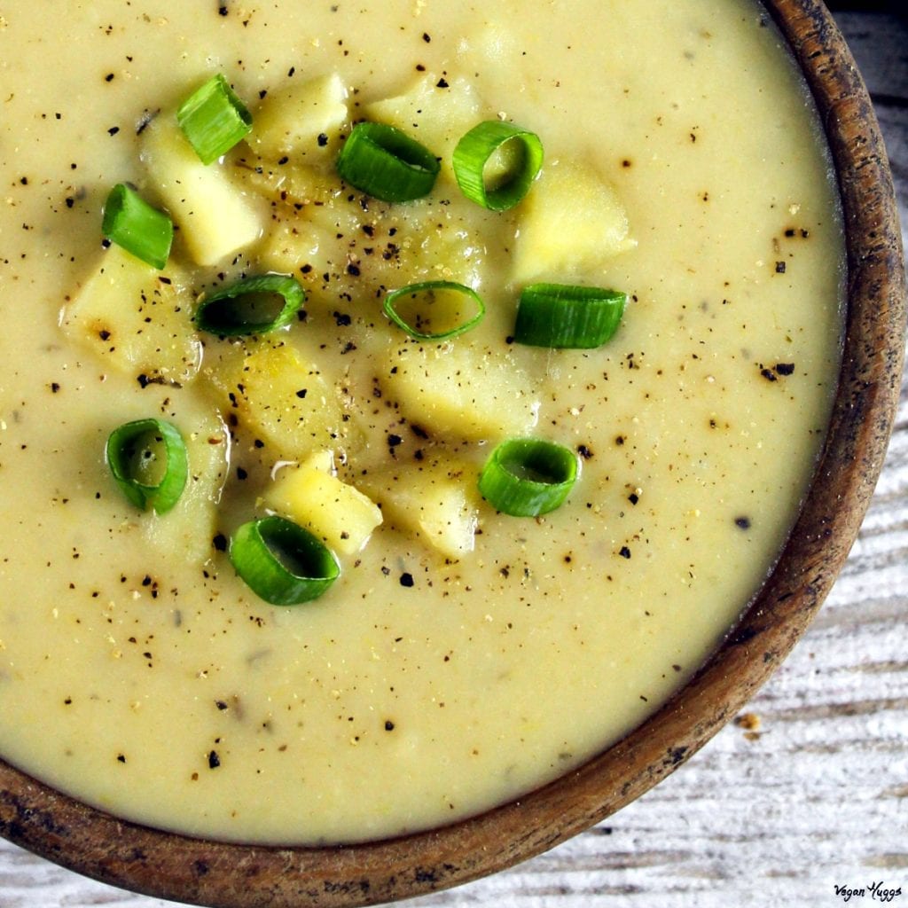 Close up photo of vegan potato leeks soup in a wooden bowl, topped with fresh green onion and black pepper. 