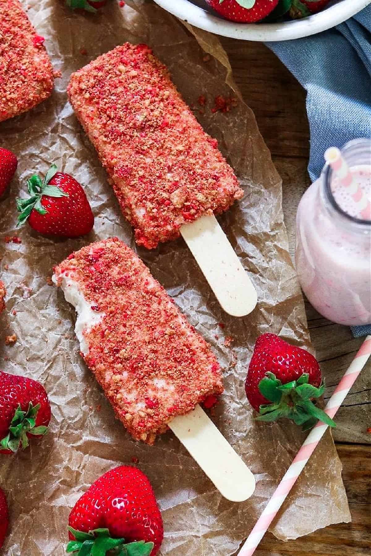 three strawberry shortcake ice cream bars on parchment paper with fresh berries on the side. 
