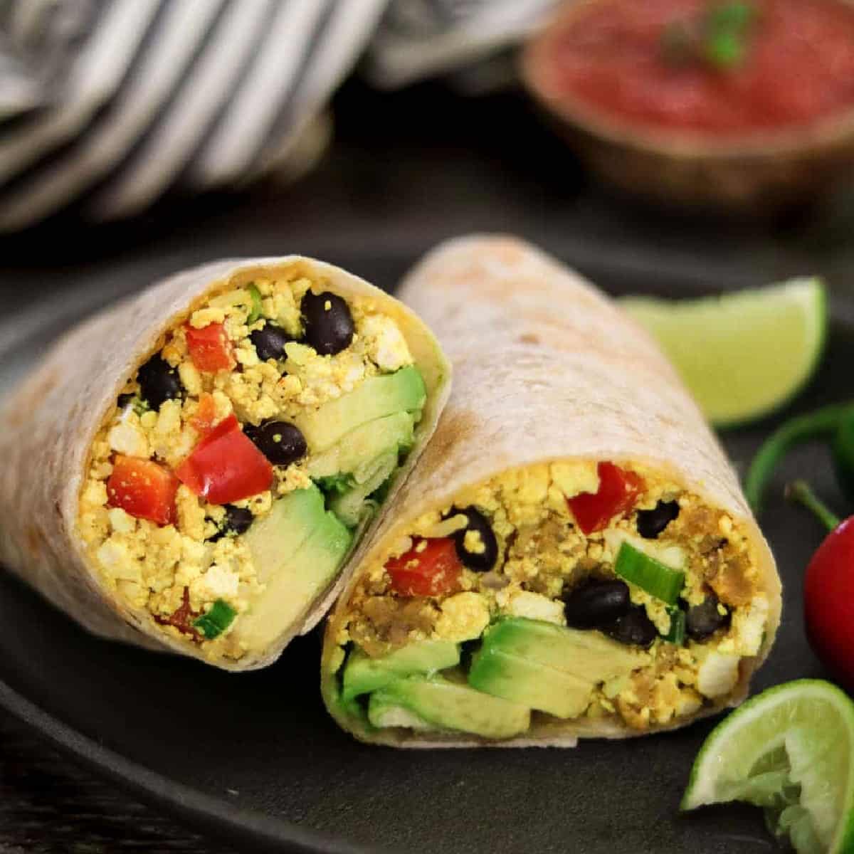 sliced burrito on a serving plate with lime and peppers on the side. 