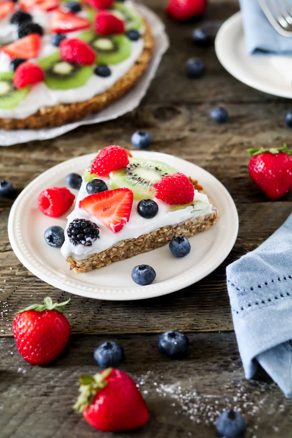 Slice of fruit pizza on a plate with fruit on the side. 