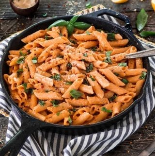 A cast iron skillet filled with roasted red pepper pasta topped with fresh basil.