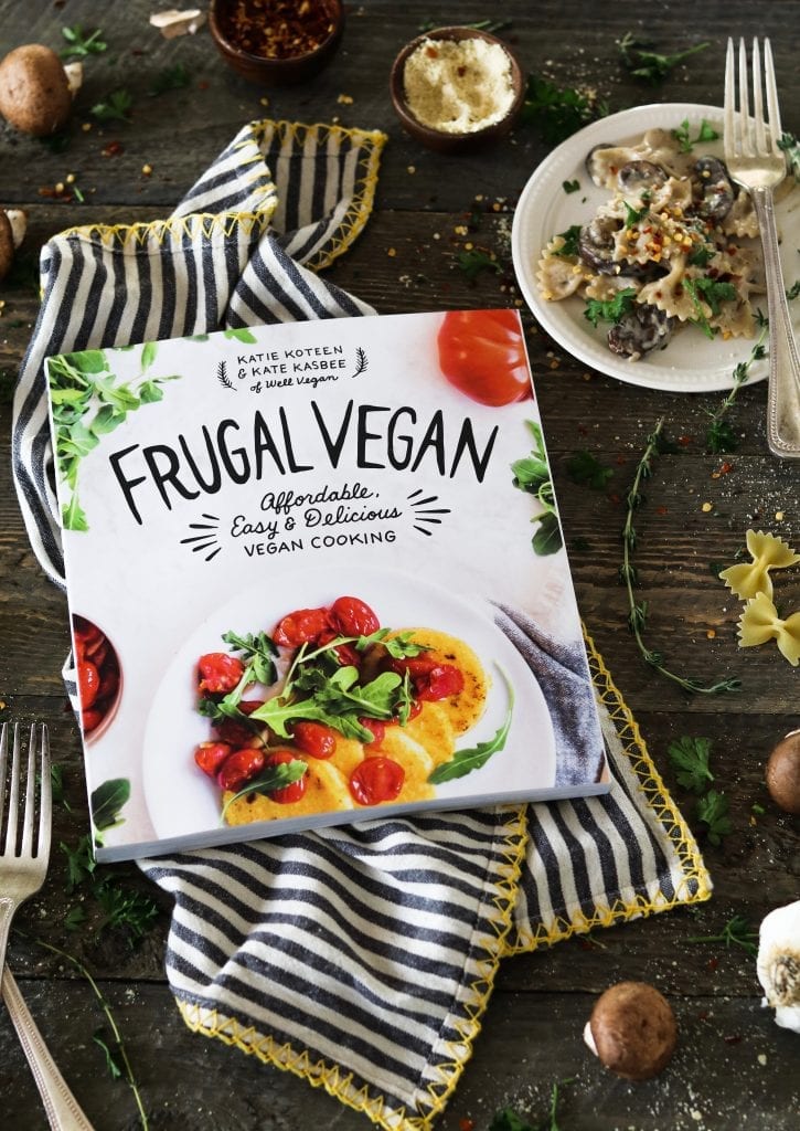 Frugal vegan cookbook on a striped napkin. Plate of vegan mushroom stroganoff on the side. 