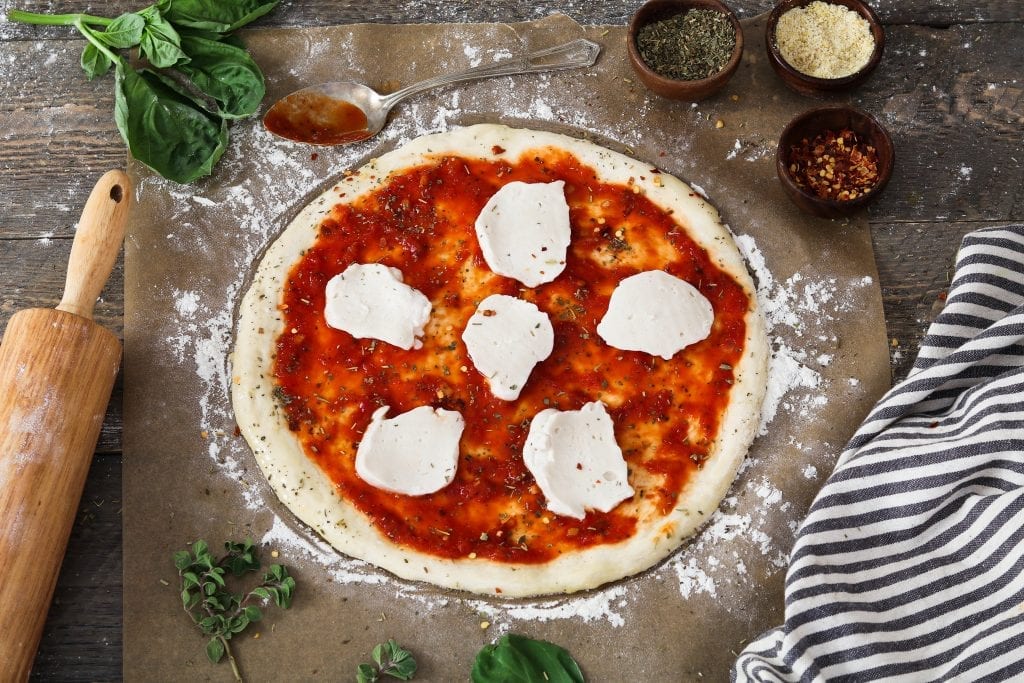 Process photo of placing vegan mozzarella cheese on top of sauce. 