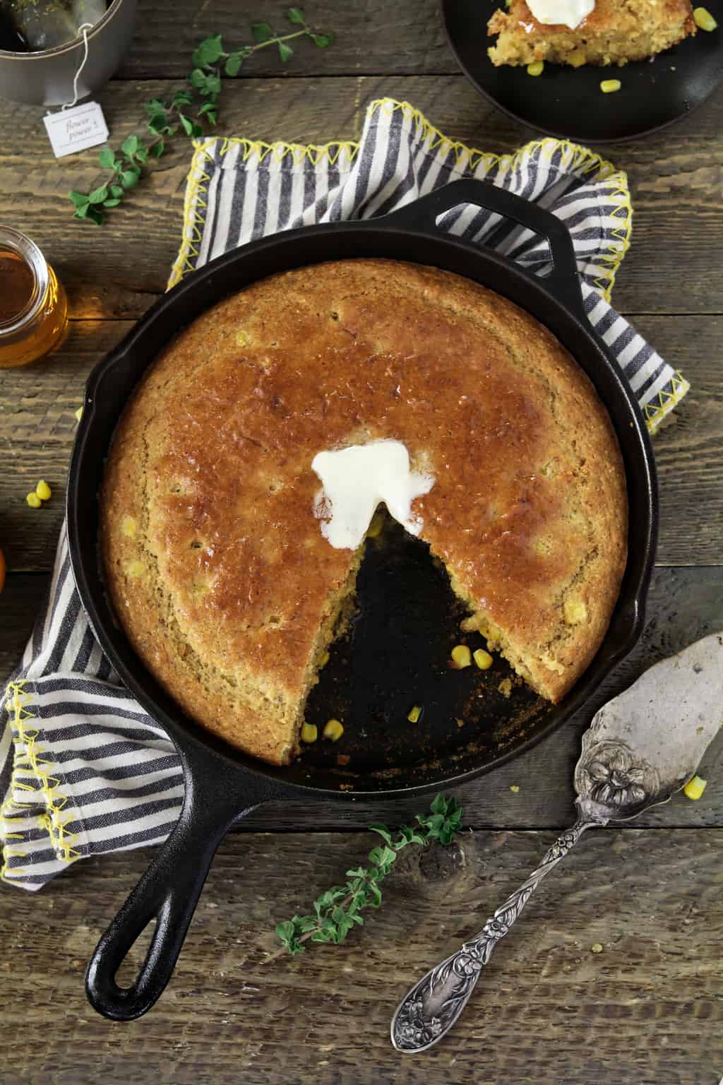 Vertical shot of Sweet Skillet Cornbread in the pan. On top of a striped napkin and maple syrup on the side. 