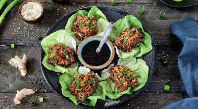 vegan lettuce wraps on a black plate. Topped with green onions, sesame seeds and carrots.