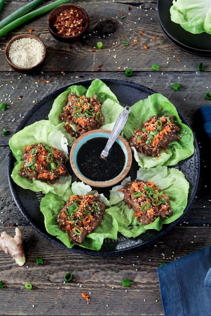 Prepared vegan lettuce wraps on a black serving plate. Topped with green onion and carrots. 