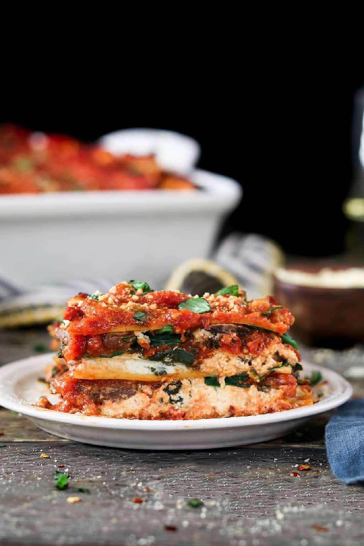 Side view of vegan lasagna on a white plate and topped with basil. 