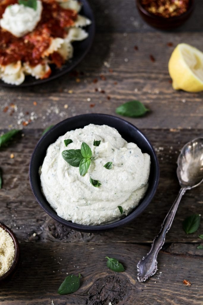Vegan Ricotta Cheese in a black bowl topped with fresh-cut basil. Spoon on the side. 