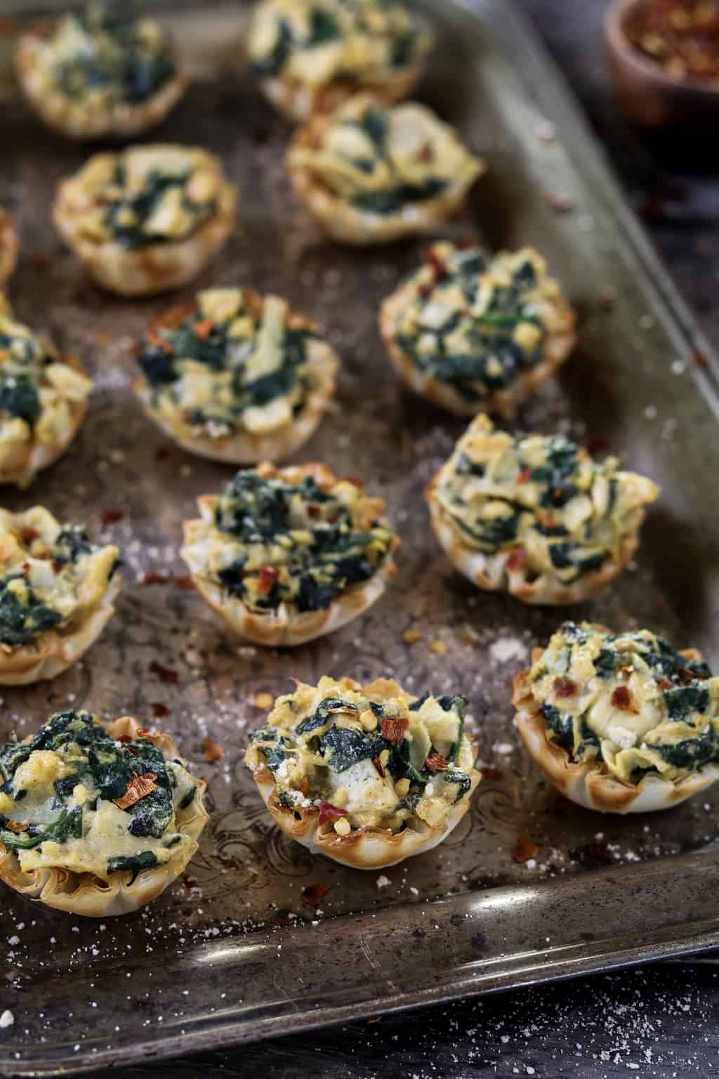 Vertical photo of fully baked Vegan Spinach Artichoke Cups on a tray.