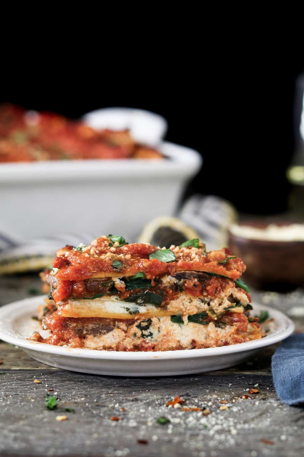 Side view of vegan mushroom lasagna on a white plate and topped with basil. 