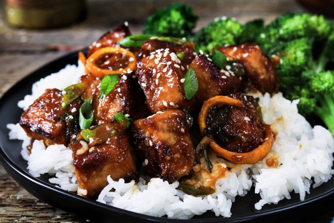 Closeup photo of General Tso's Tofu on a bed of rice with a side of broccoli. 