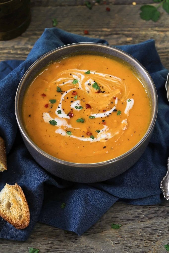 Grey bowl of vegan carrot ginger soup topped with coconut milk, cilantro and red pepper flakes. 