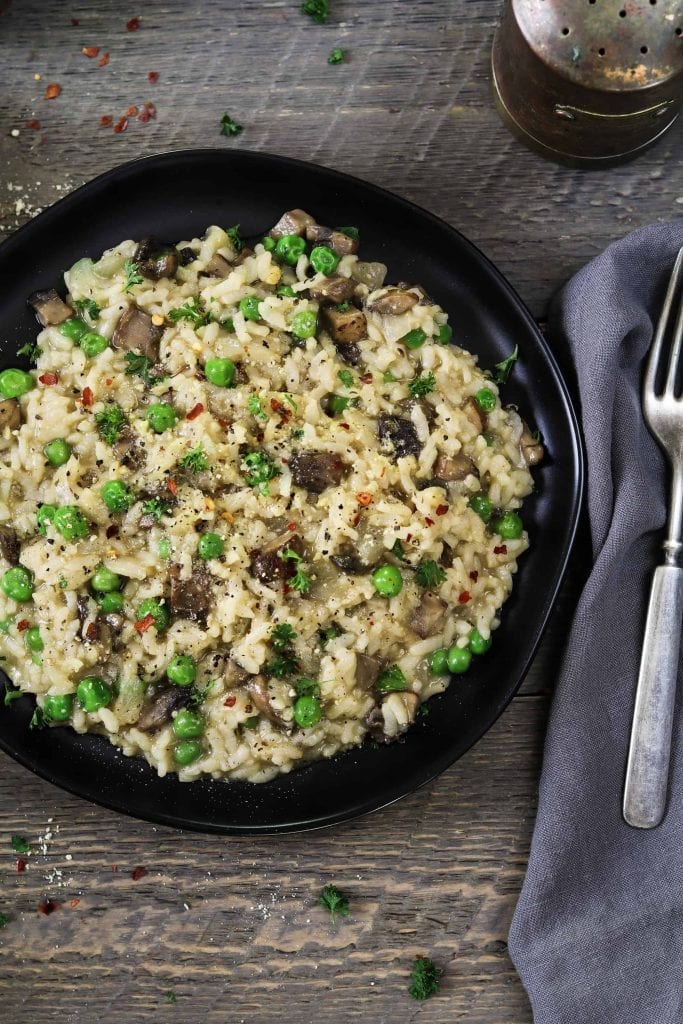 Overhead shot of instant pot mushroom risotto on a black plate. Grey napkin on the side with silver fork. 