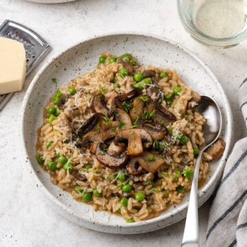 instant pot mushroom risotto in a white bowl with a spoon on the side.