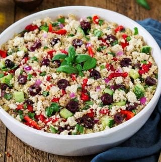 Mediterranean Quinoa Salad in a white bowl with bottle of olive oil on the side.