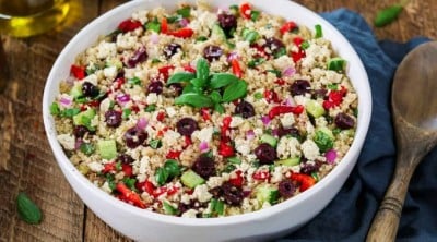Mediterranean Quinoa Salad in a white bowl with bottle of olive oil on the side.