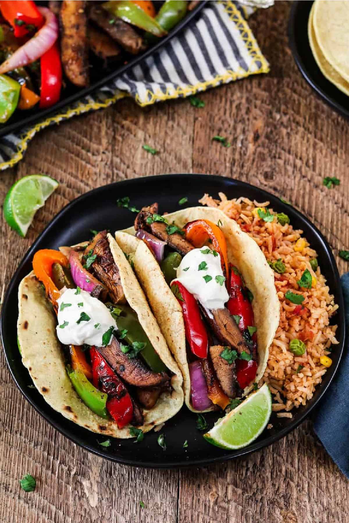 Get your weeknight sizzling In just 30 minutes with these Portobello Vegan Fajitas. They are spicy, smoky, subtly sweet and robust! The flavors come together when the seared veggies meet the homemade fajita sauce. It's mouth-watering good! 2 vegan fajitas on a black plate with rice on the side.
