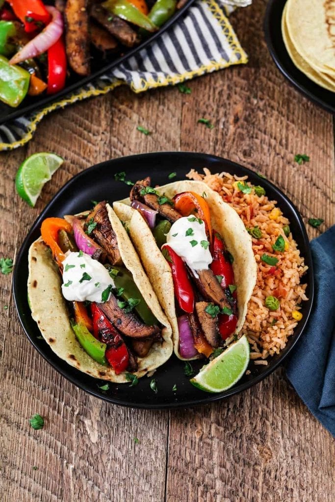 2 vegan fajitas on a black plate. Side of lime with blue napkin. 