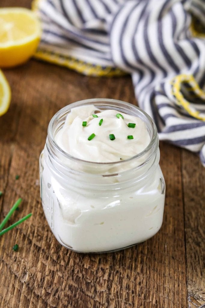 small jar filled with vegan sour cream recipe. Topped with fresh-cut chives. Striped napkin in the background. 