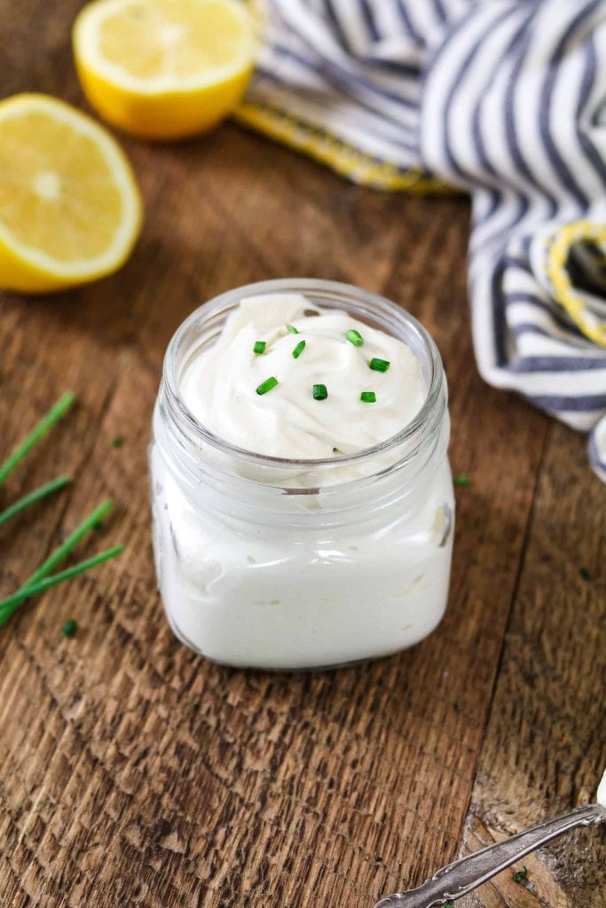 small jar filled with sour cream. Two lemon halves in the background.