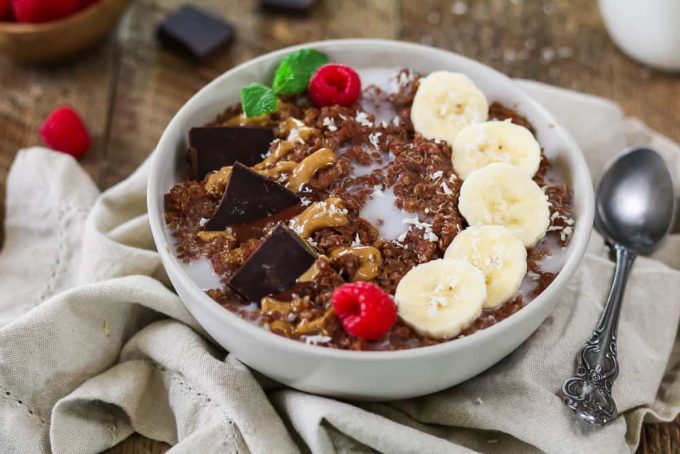 Breakfast quinoa bowl with spoon on the side. Topped with bananas, chocolate and peanut butter. 