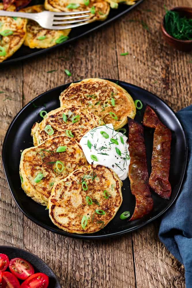 vegan savory pancakes on a black plate. Topped with vegan sour cream and a side of vegan bacon