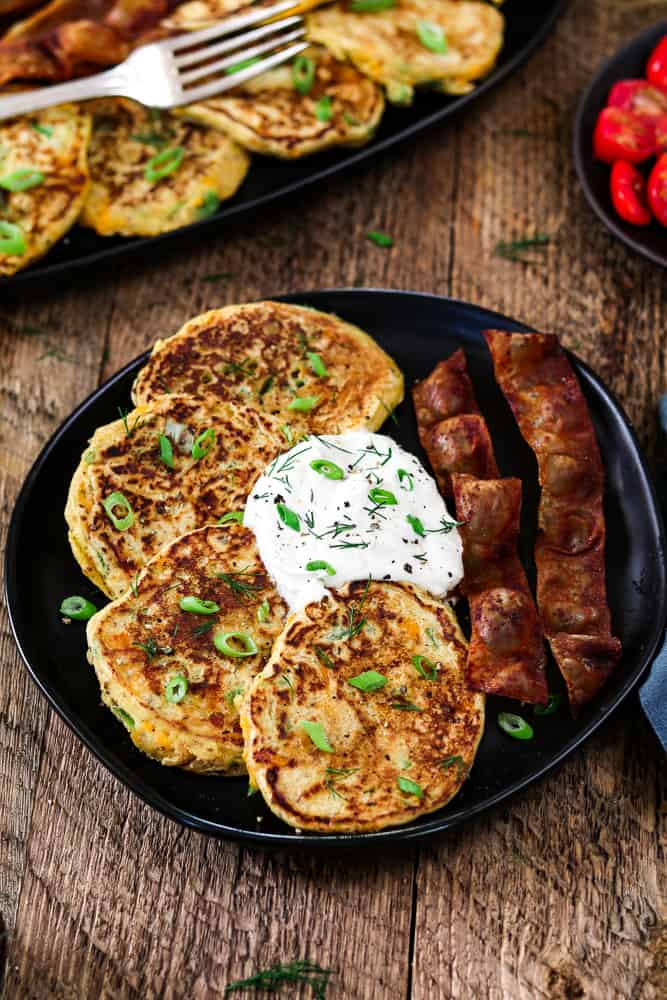 Plate of savory pancakes with a plate of pancakes in the background. Tomatoes and blue napkin on the side. 