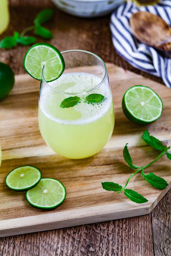 A glass of fresh limeade on a wood cutting board. Fresh mint and lime wedges on the side. 