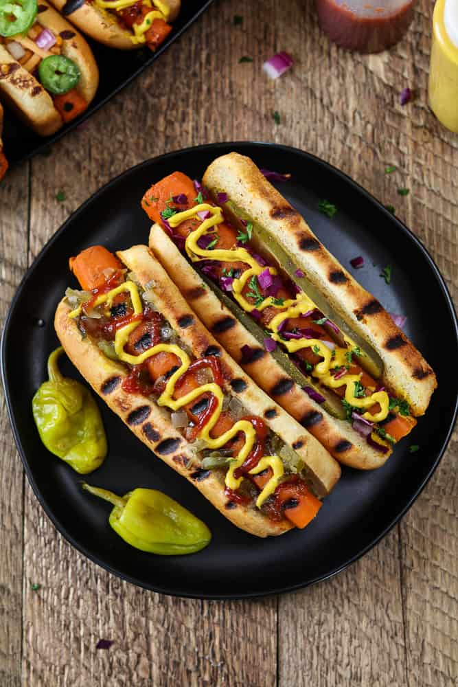 Two Vegan Carrot Hot Dogs on a black plate. Topped with mustard and ketchup. 