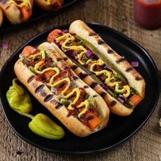 Two Vegan Carrot Hot Dogs on a plate with two pepperoncinis on the side.